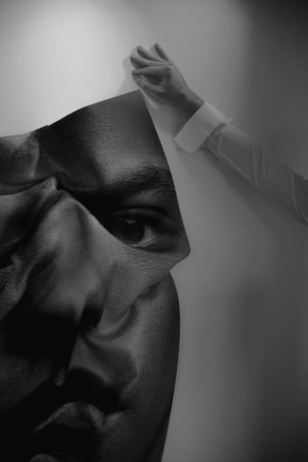 Close-up of a person holding a large black and white poster of a face, with an attachment that looks like part of a medical or artistic installation.