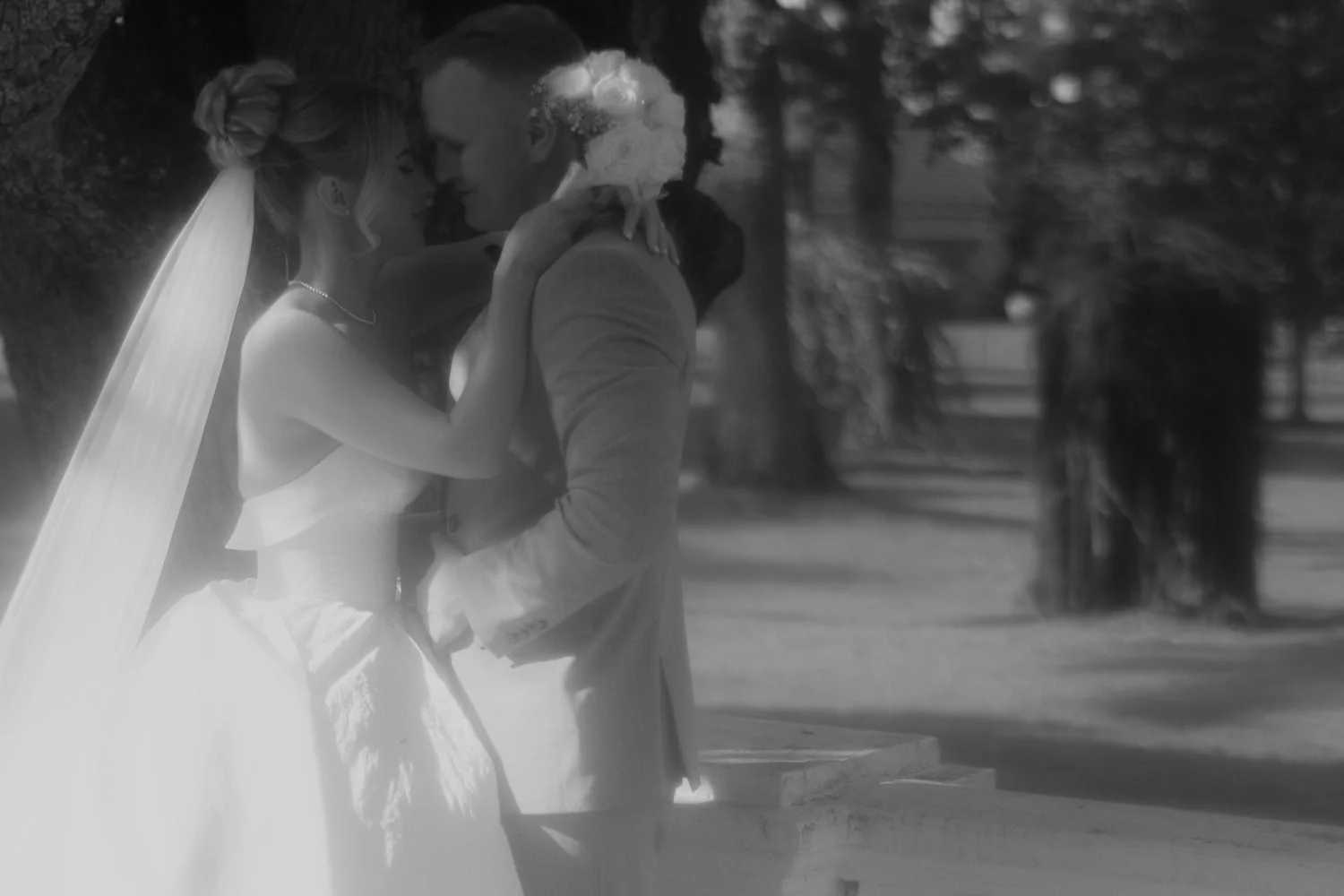 A bride and groom share a romantic moment outdoors, with trees and a park in the background, during their wedding