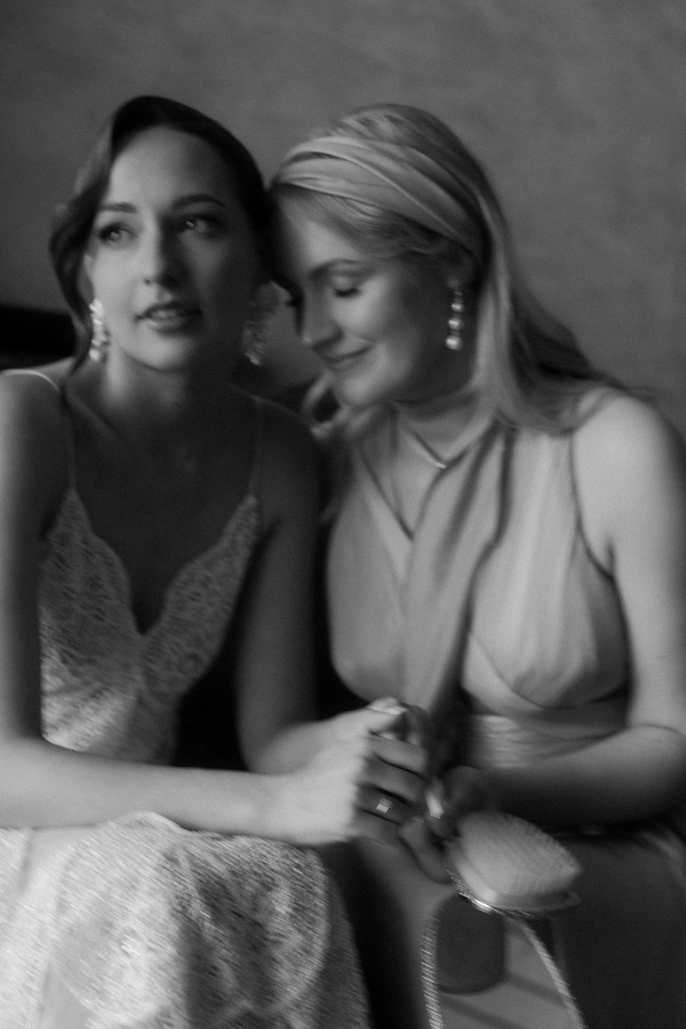 Two women dressed elegantly, sitting close together, smiling and holding a glass of wine