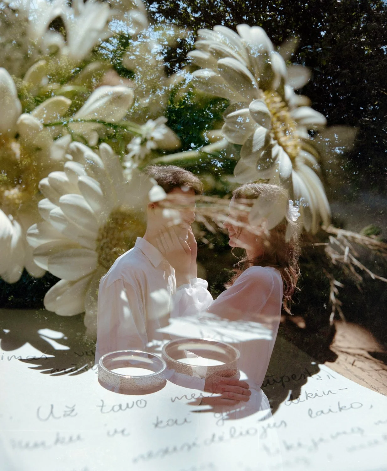 A double exposure photo combining a close-up of white daisy flowers with a elope couple smiling and touching faces outdoors, along with handwritten text at the bottom.