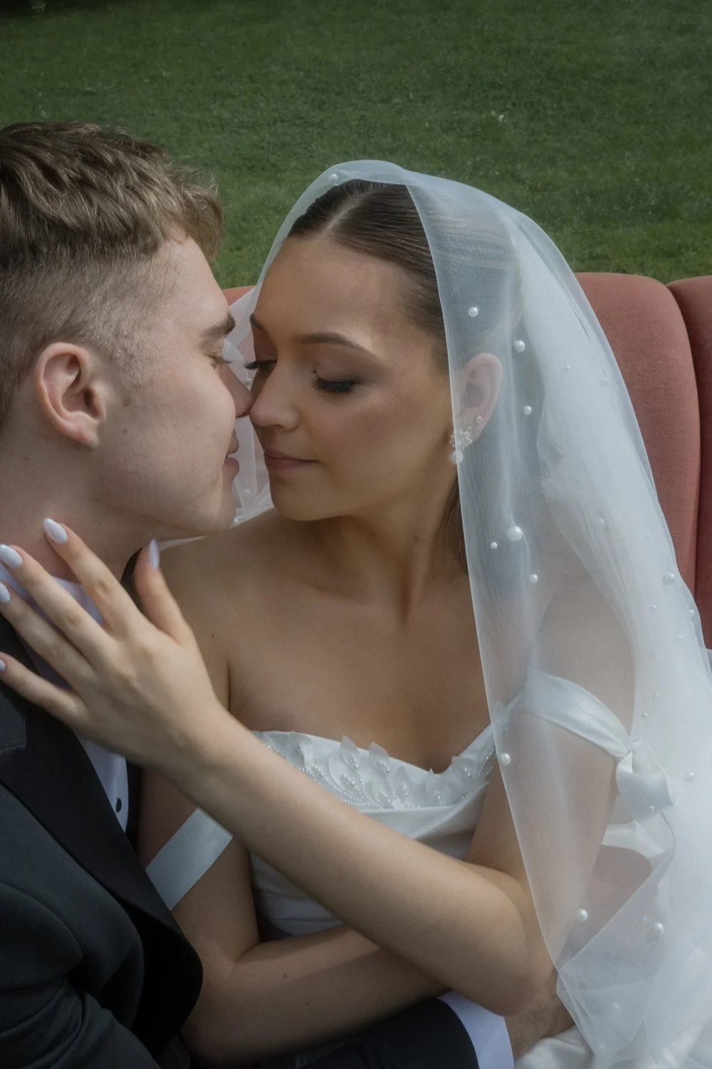 A bride and groom close up, about to kiss, with a green outdoor background.