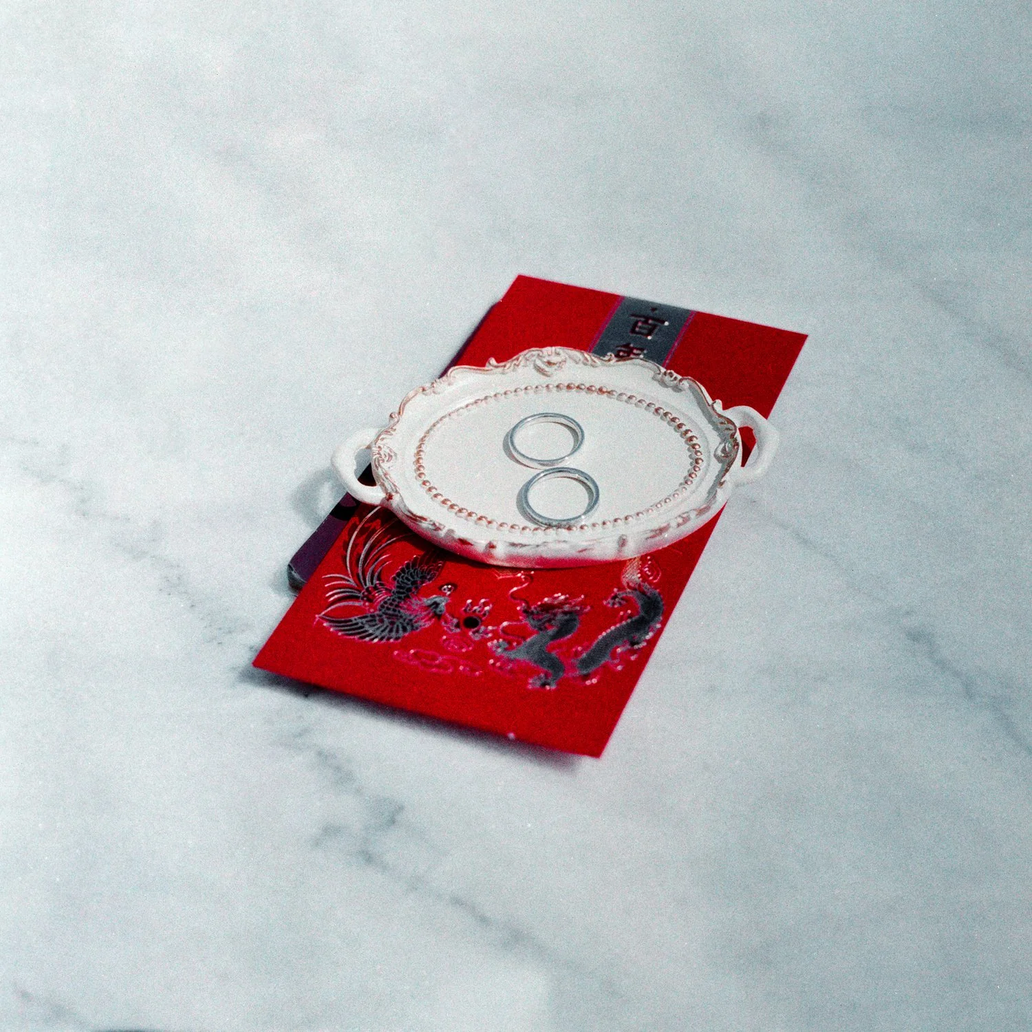 A decorative white tray with cut-out handles on a red and black paper with a dragon and phoenix design, placed on a white marble surface.