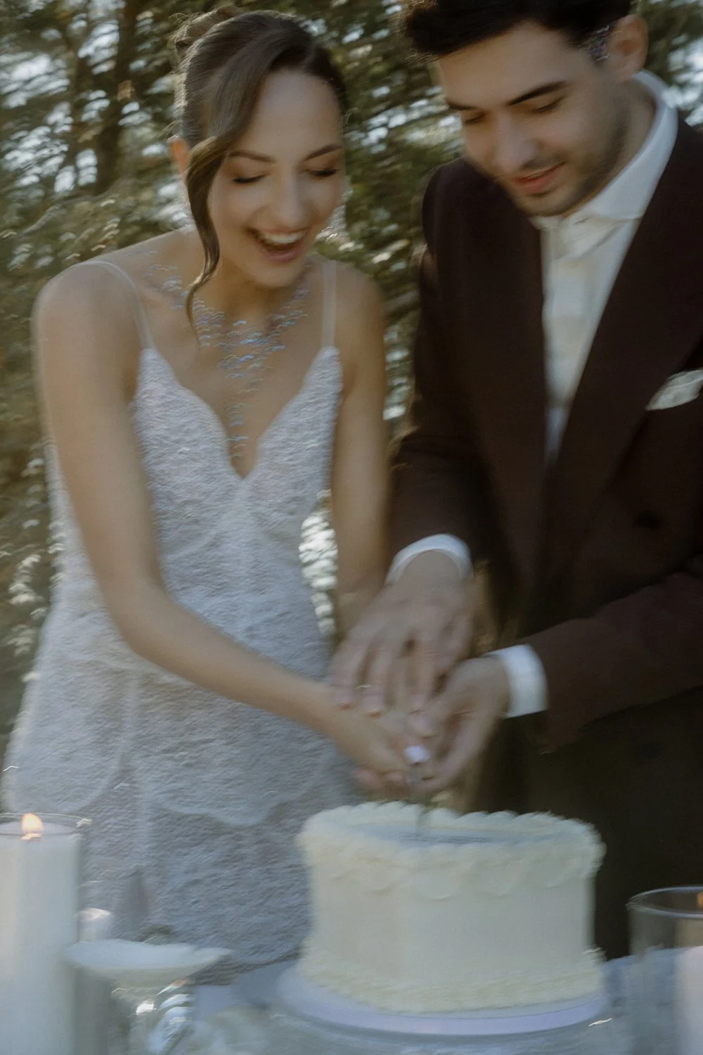 A bride and groom cutting a wedding cake together outdoors during daytime.