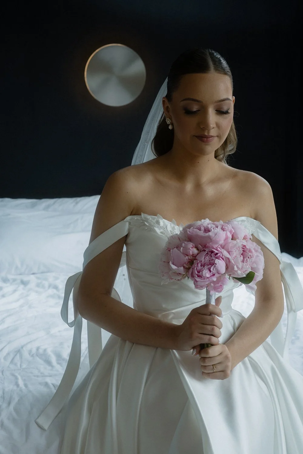 A bride in a white wedding dress holding a pink bouquet of flowers in a dimly lit room.