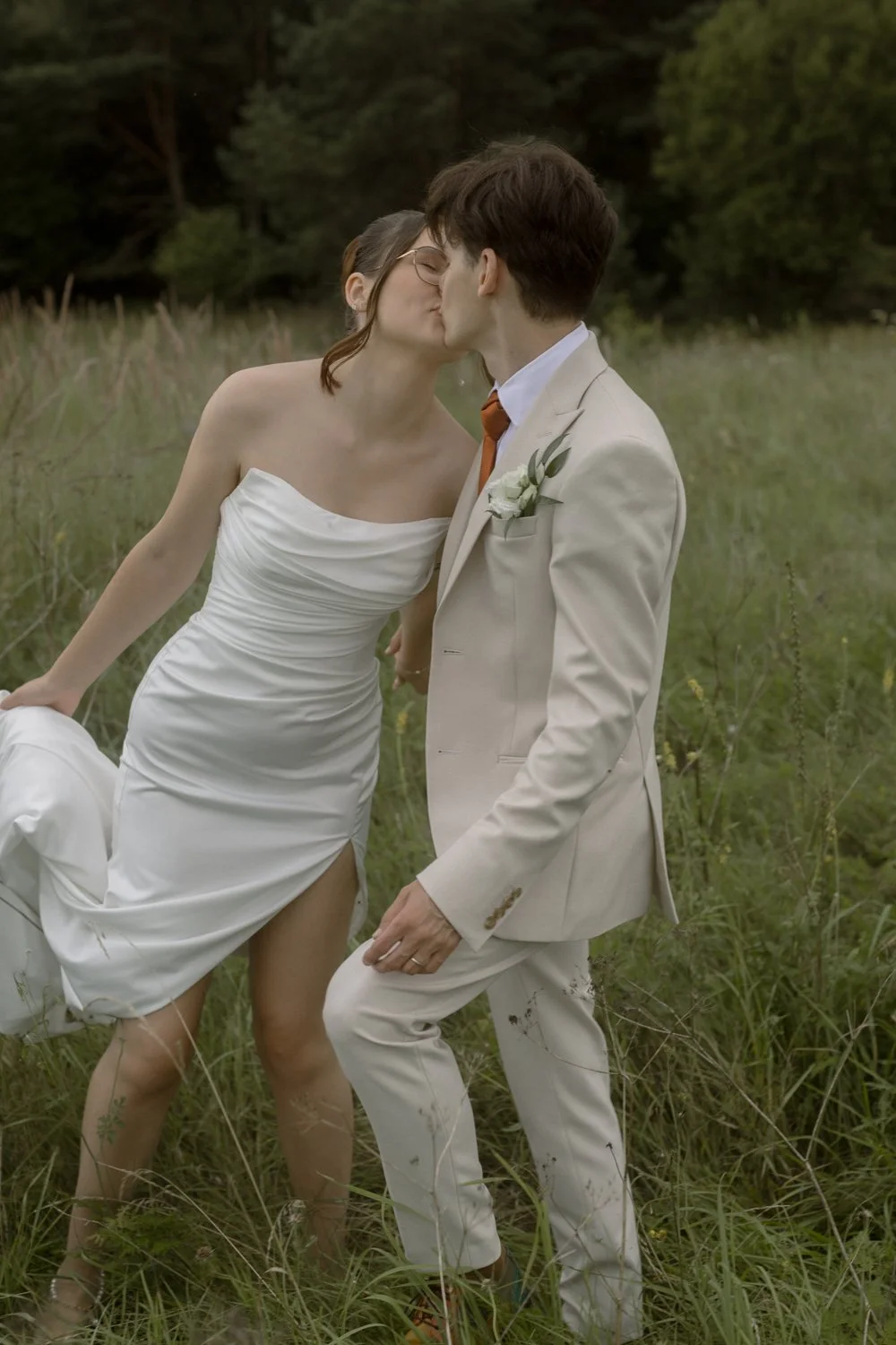 A couple dressed in wedding attire kissing in a grassy field.