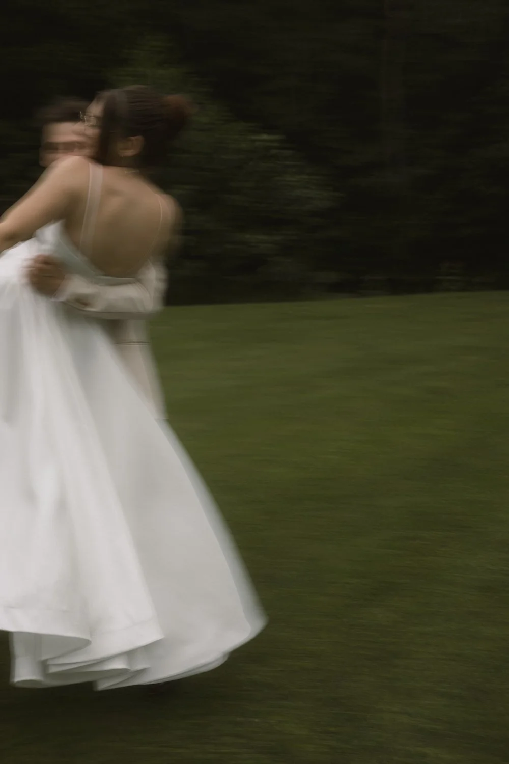 A woman in a white dress spinning outdoors with a blurred background of trees.