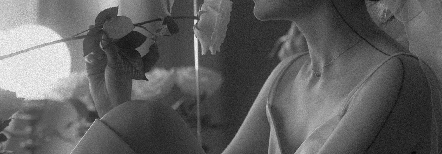 Close-up of a woman holding a flower, with focus on her face and shoulder, in black and white.