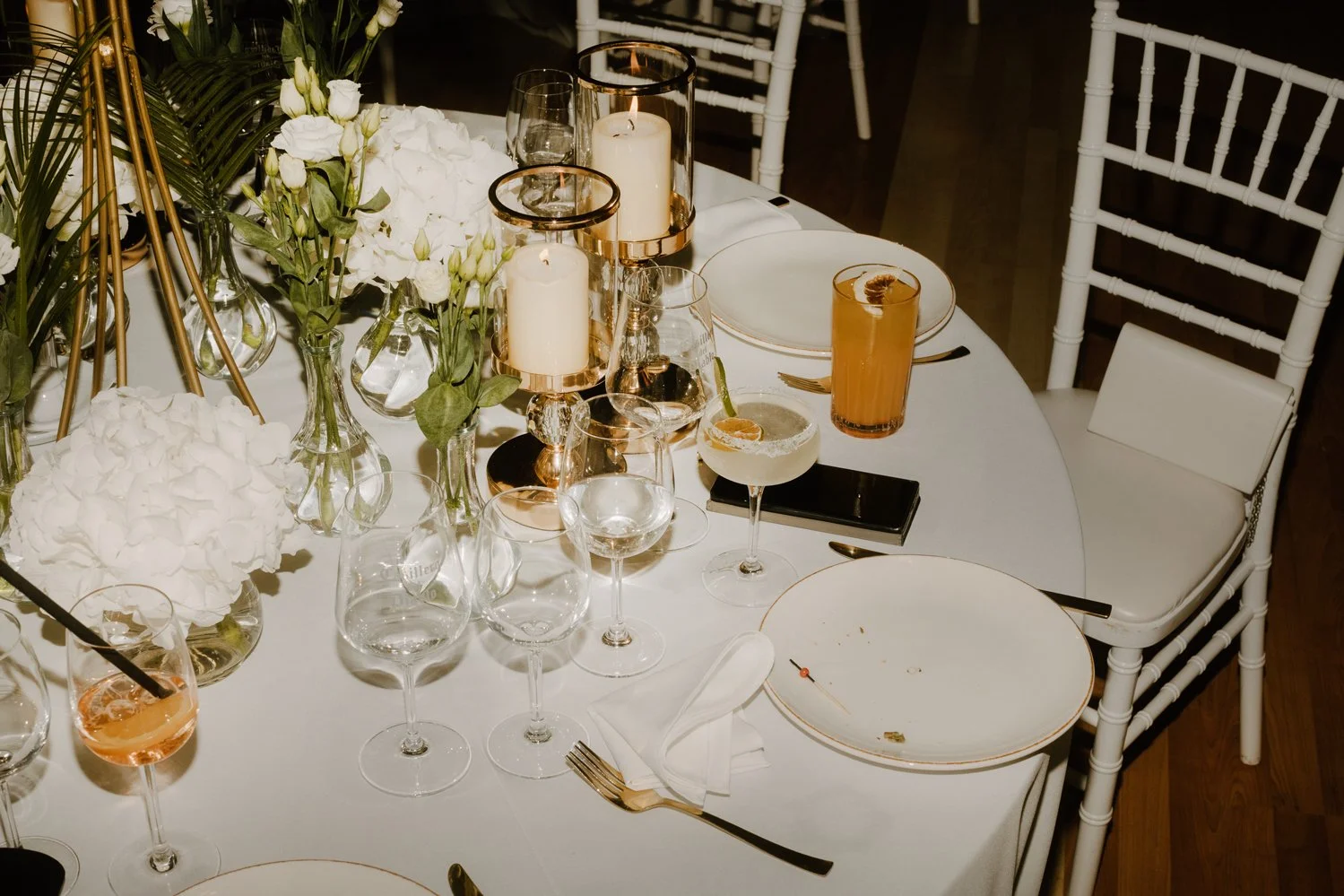 Elegant dining table with white tablecloth, floral centerpieces, candles, and assorted drinks, set for a special occasion.