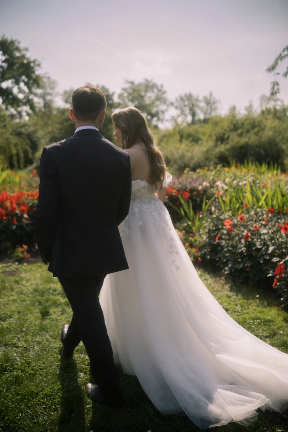 A bride and groom walking in a garden with colorful flowers, with the bride wearing a white gown and the groom in a black suit.