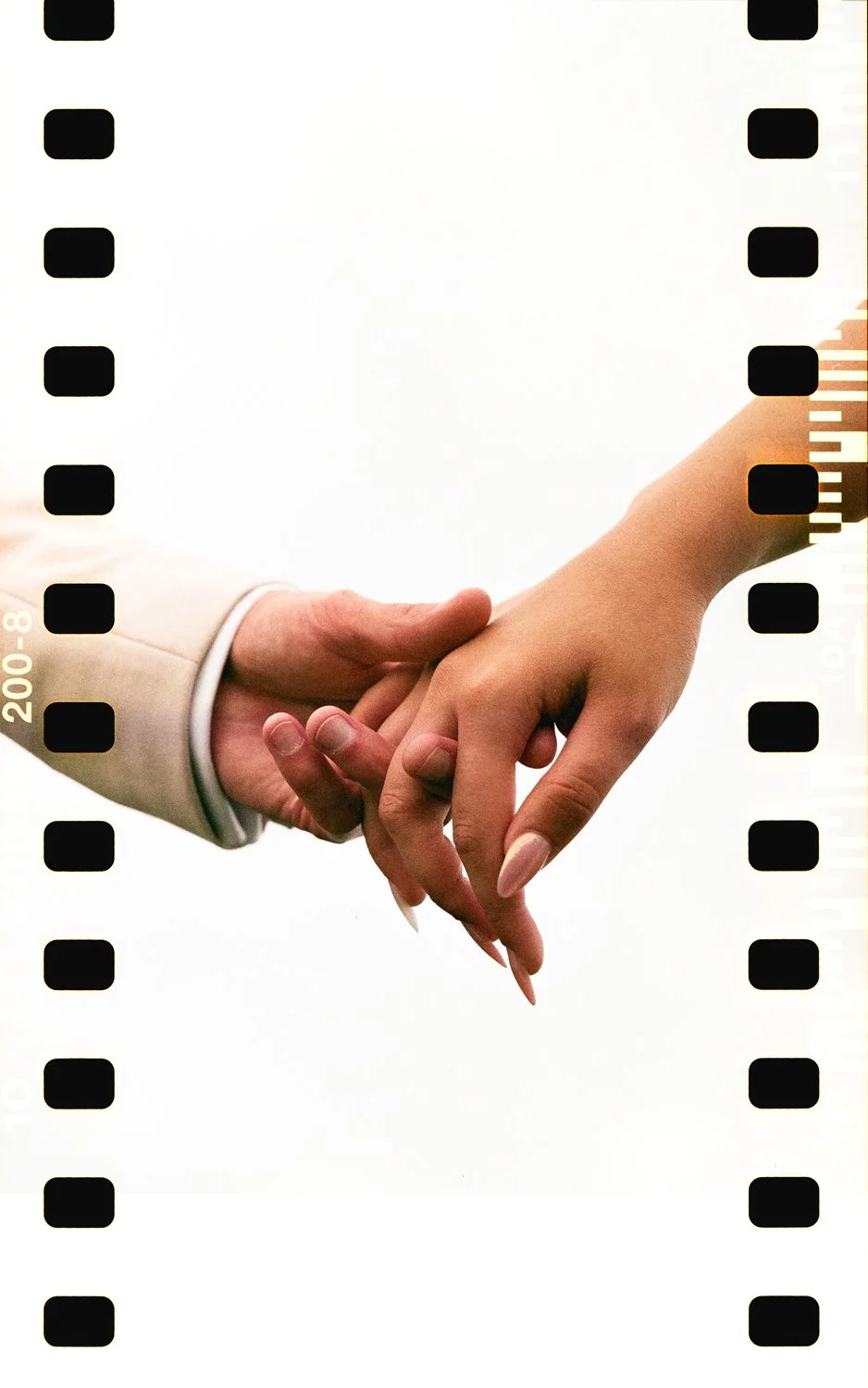 Close-up of a man and woman holding hands, fingers intertwined, against a plain white background.