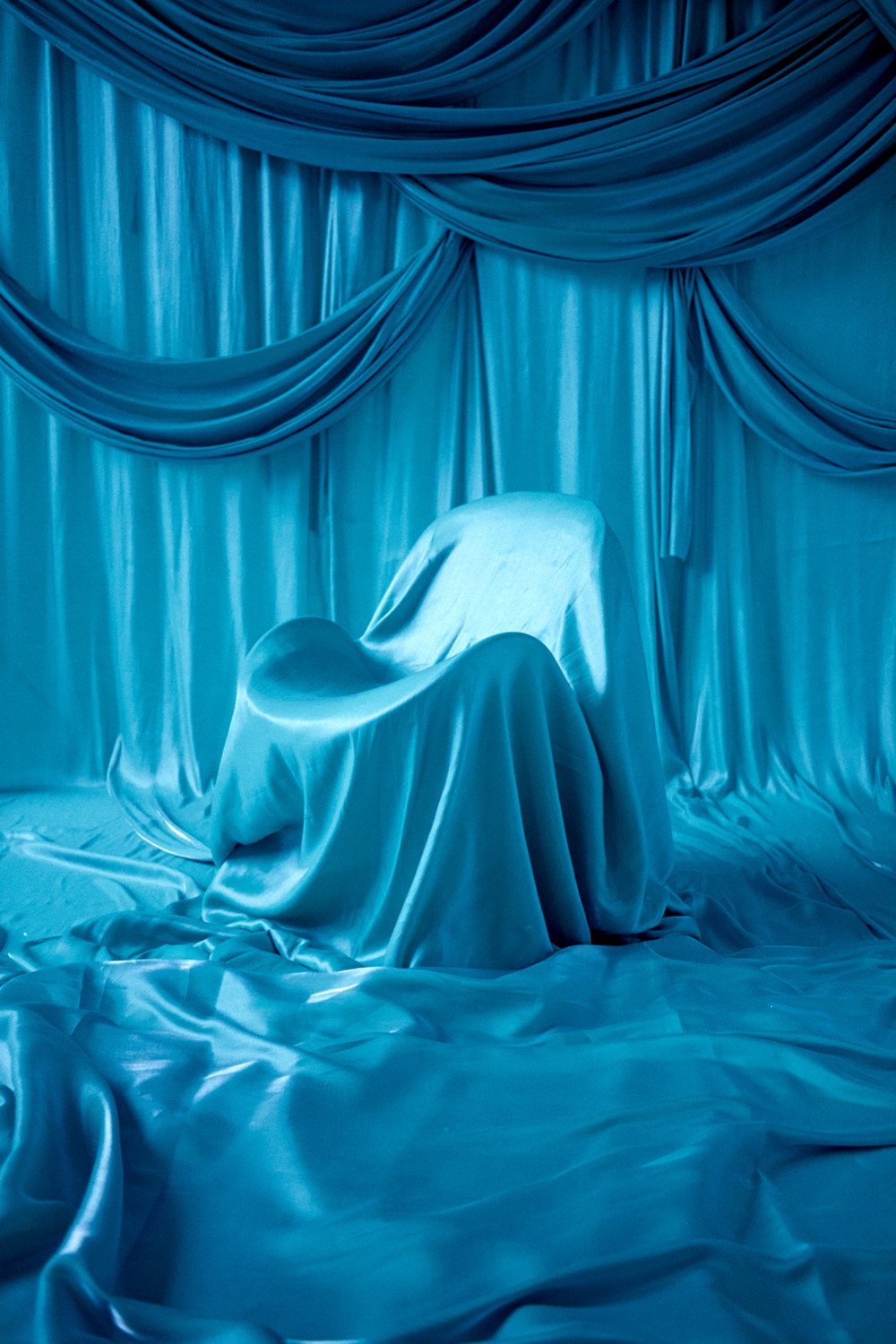 A chair covered with satin fabric is set in front of gathered satin curtains in shades of blue.