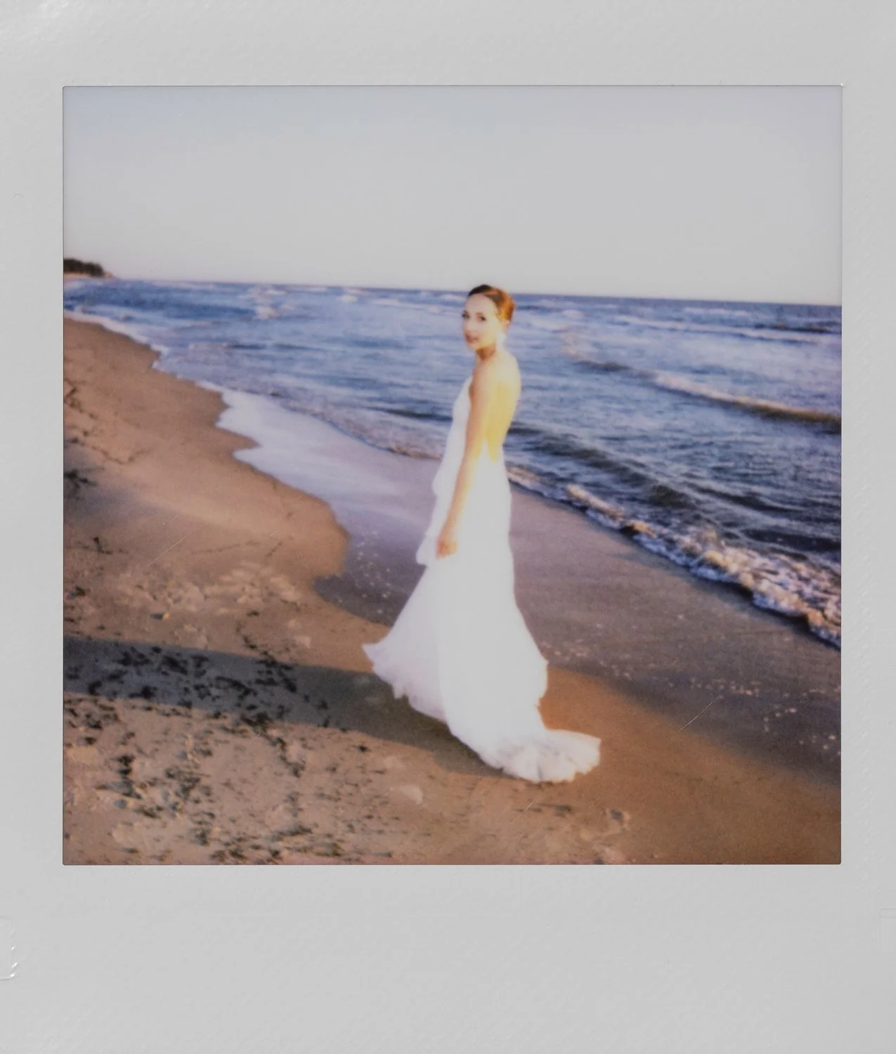 A woman in a white dress standing on a beach with ocean waves in the background.