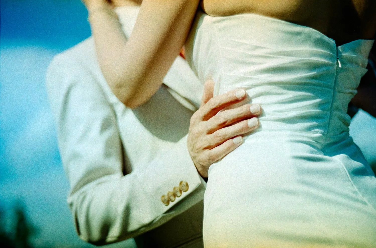 A close-up of a couple dancing, focusing on their torsos and hands, with the woman wearing a strapless satin dress and the man in a suit with a white shirt.