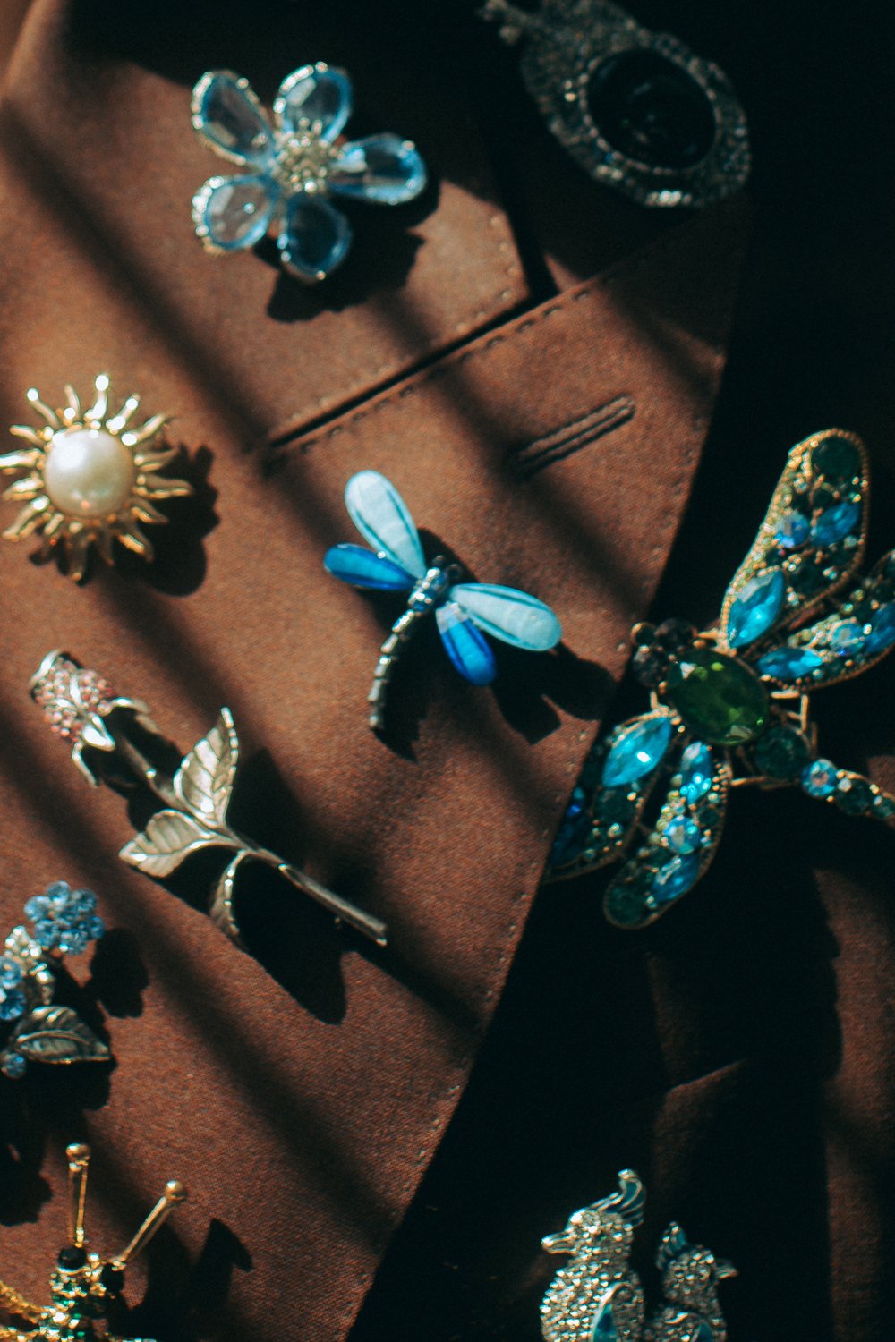 Assorted earrings and brooches with floral, butterfly, and dragonfly designs on a brown fabric background.