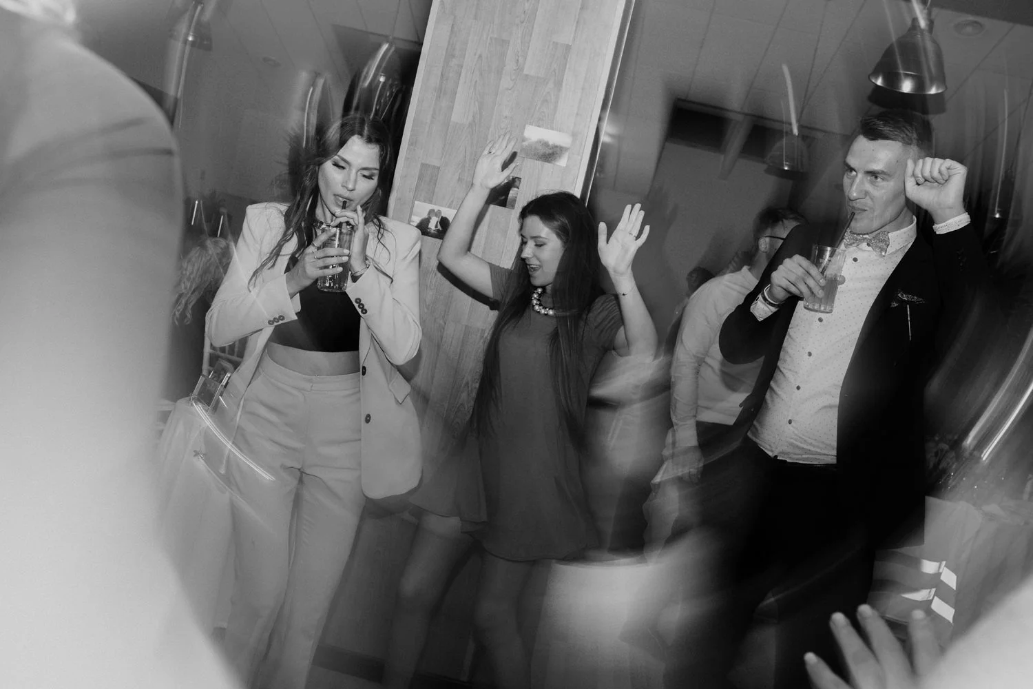 People dancing and socializing at a party or gathering, some holding drinks, in an indoor setting.