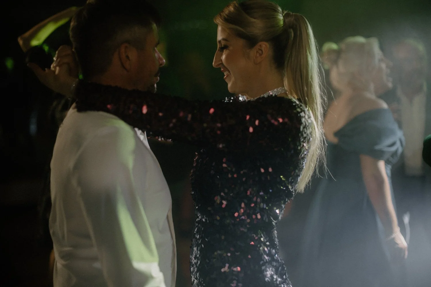 A man and a woman dancing closely together at a party or dance event, with other people in the background.