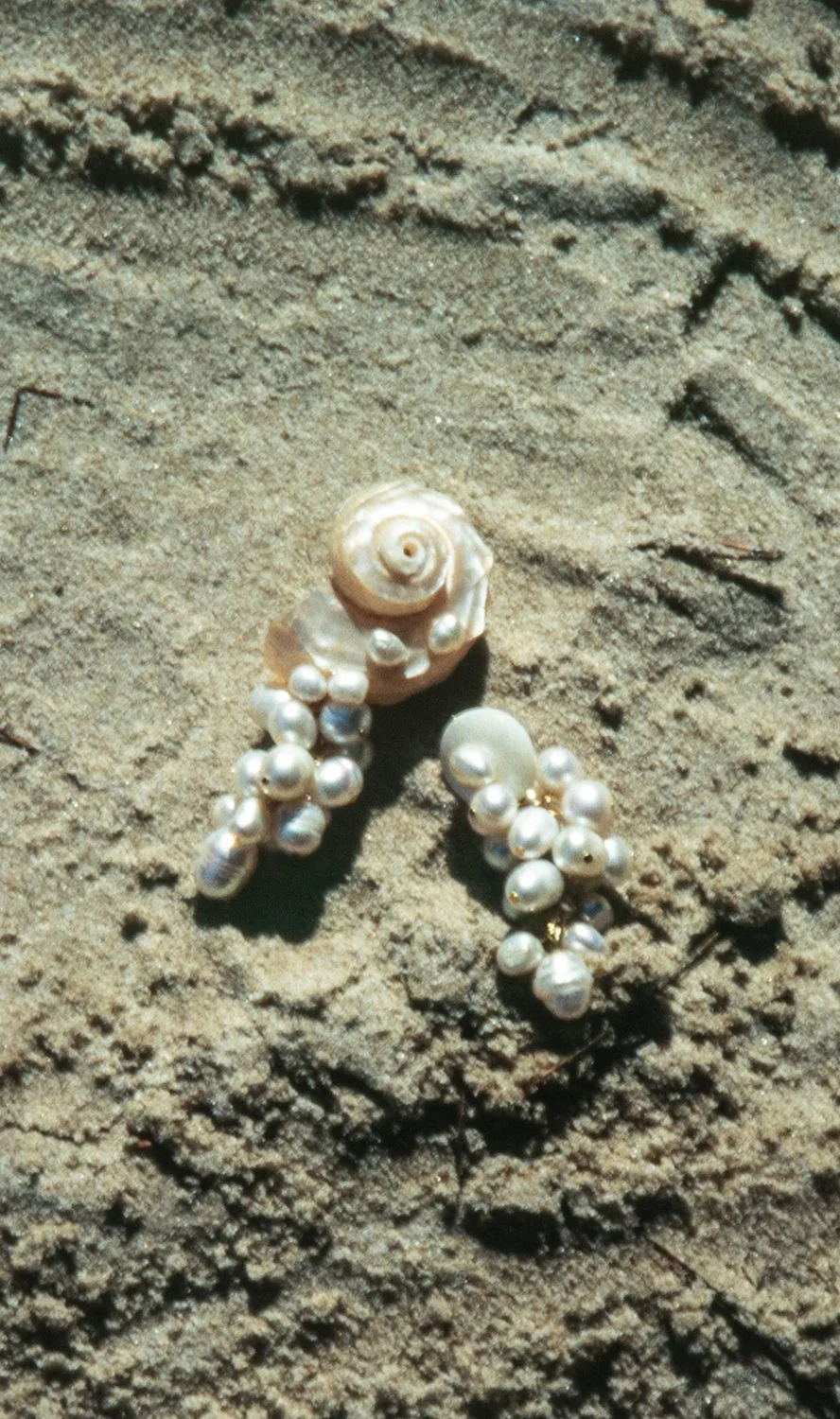 A collection of white pearl-like beads and shells arranged on sandy ground.