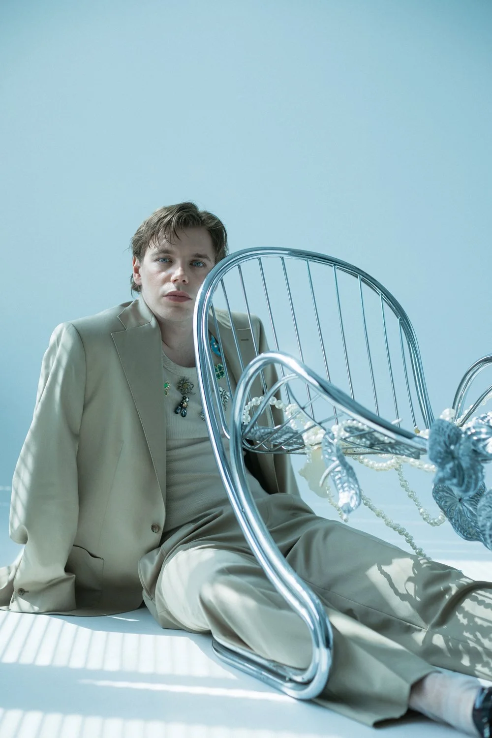 A man in a beige suit sitting on the floor next to a shattered, ornate glass chair.