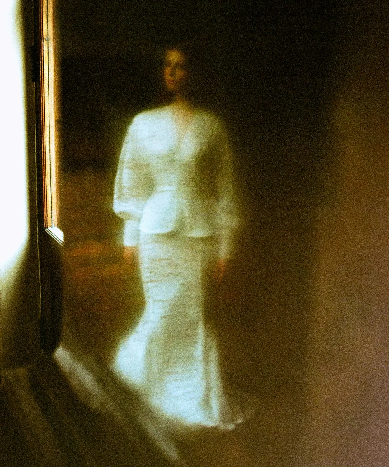 A woman standing in front of a mirror, wearing a white jacket and pants, with a dark background.