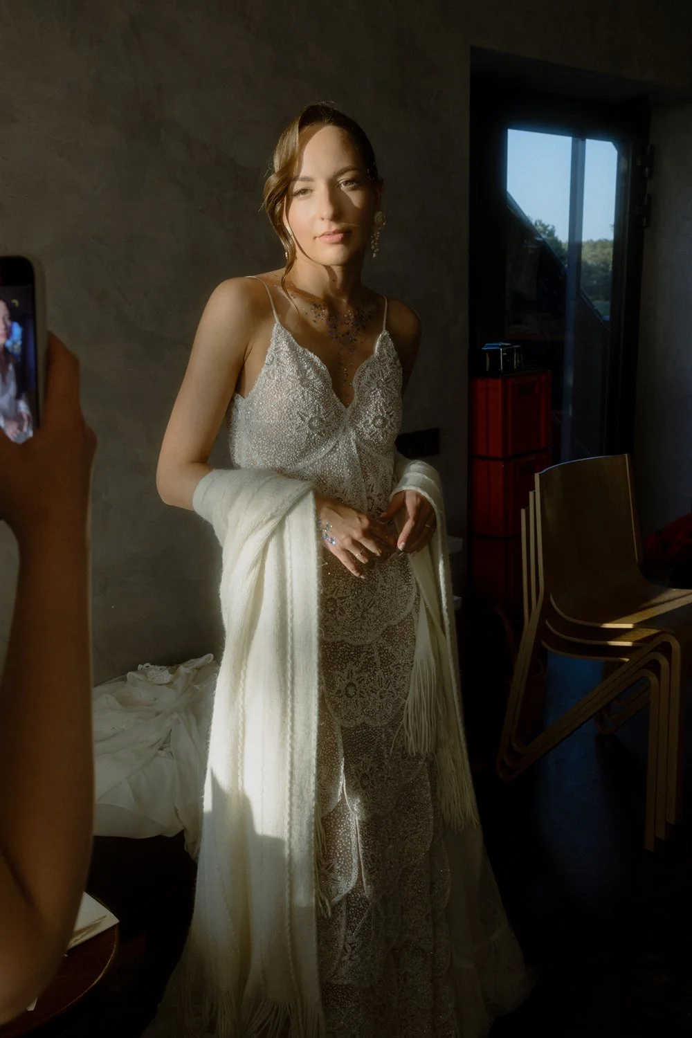 A woman wearing a silver, lace, and beaded dress with a white fringe shawl, standing in a dimly lit room.