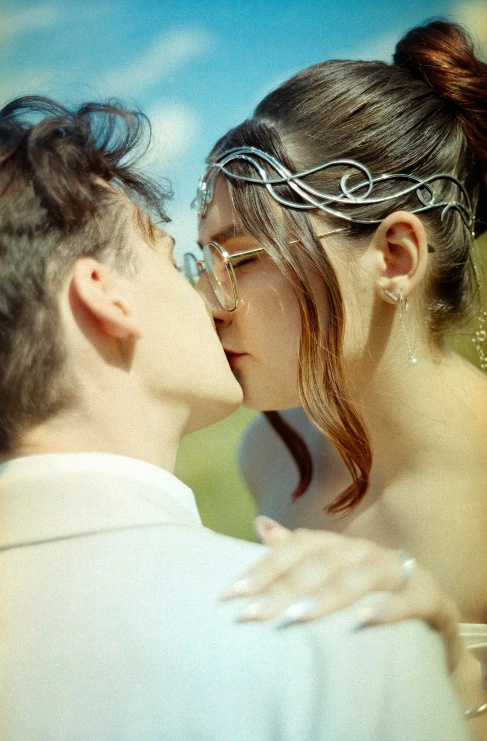 A couple sharing a kiss, outdoors on a sunny day, with a blurred background.