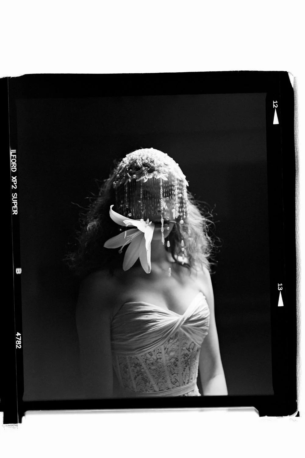 Black and white photograph of a woman with a floral headpiece and veil, wearing a strapless lace dress.