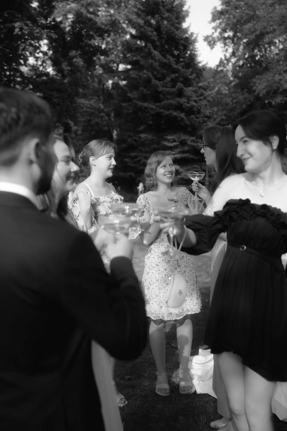 People gathered outdoors at a social event, holding glasses, with trees in the background.