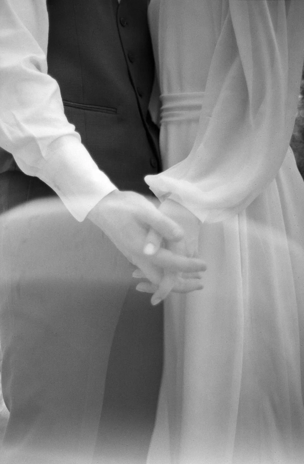 A black-and-white photo of a bride and groom holding hands, with the bride wearing a white dress and the groom in a dark suit.