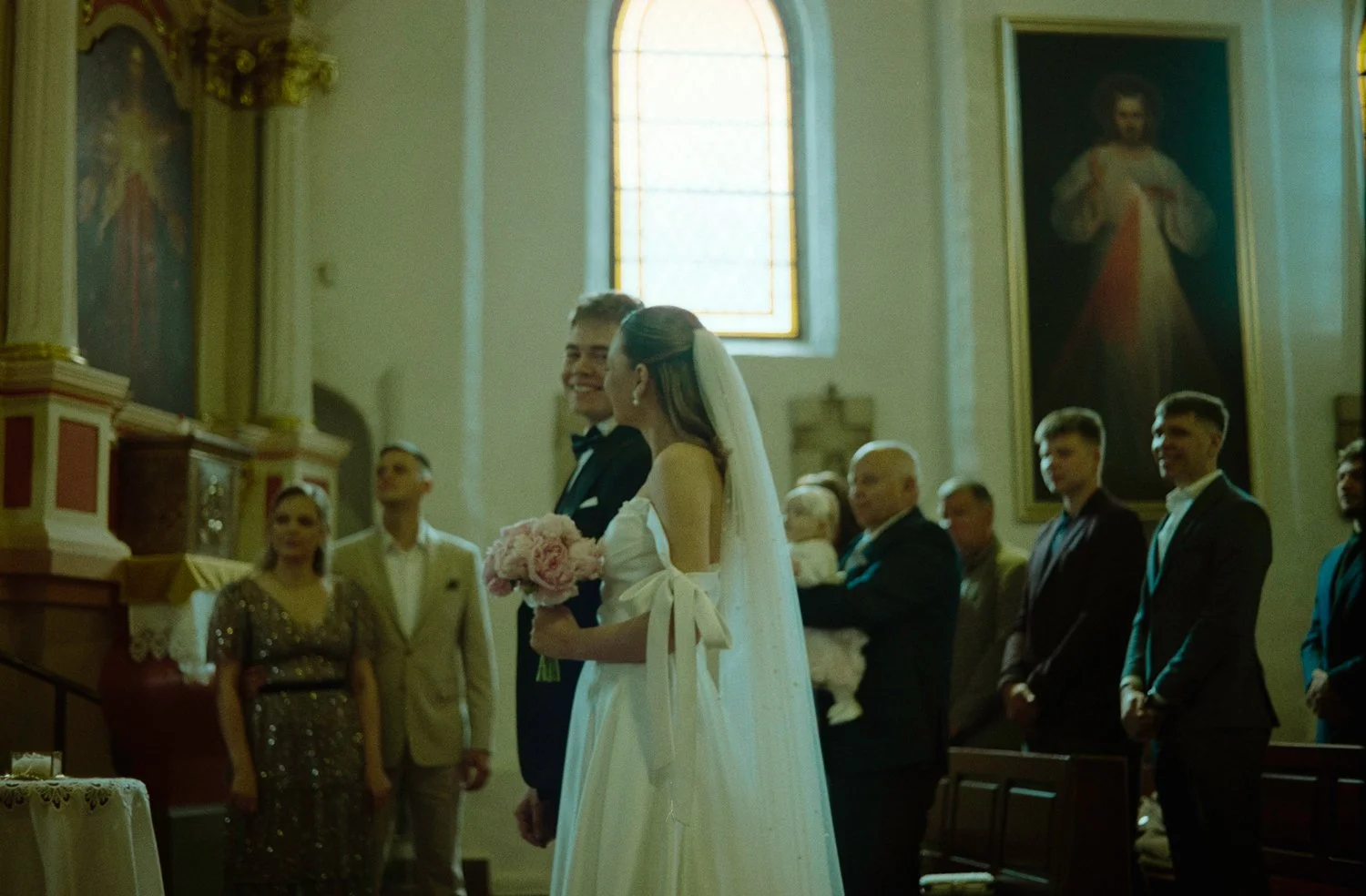 A bride and groom standing at the altar during a wedding ceremony inside a church, with wedding guests observing.