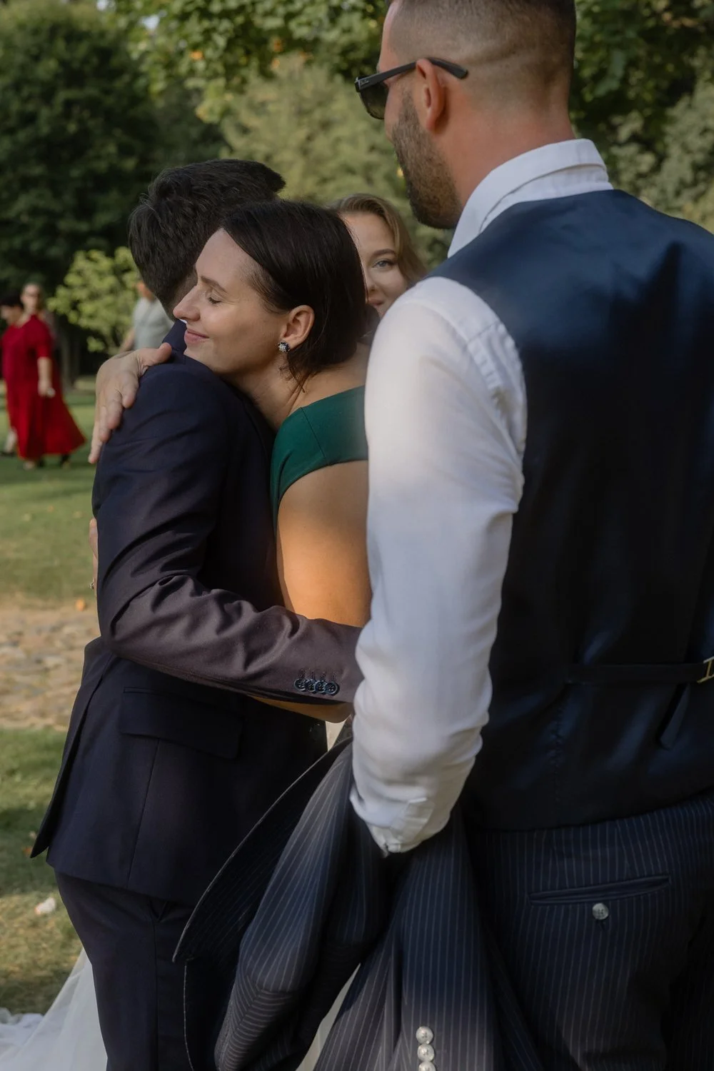 A woman and a man hugging at an outdoor event with others in the background, trees, and grass.