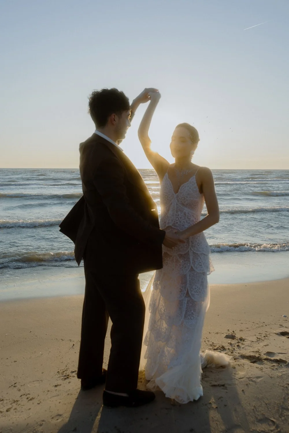 A couple in wedding attire dancing on the beach during sunset