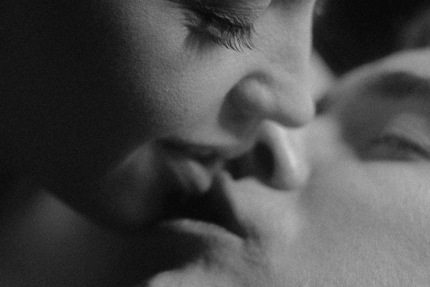 Close-up of a person's face in black and white, showing their eyes, nose, and partially closed lips with hand touching face.