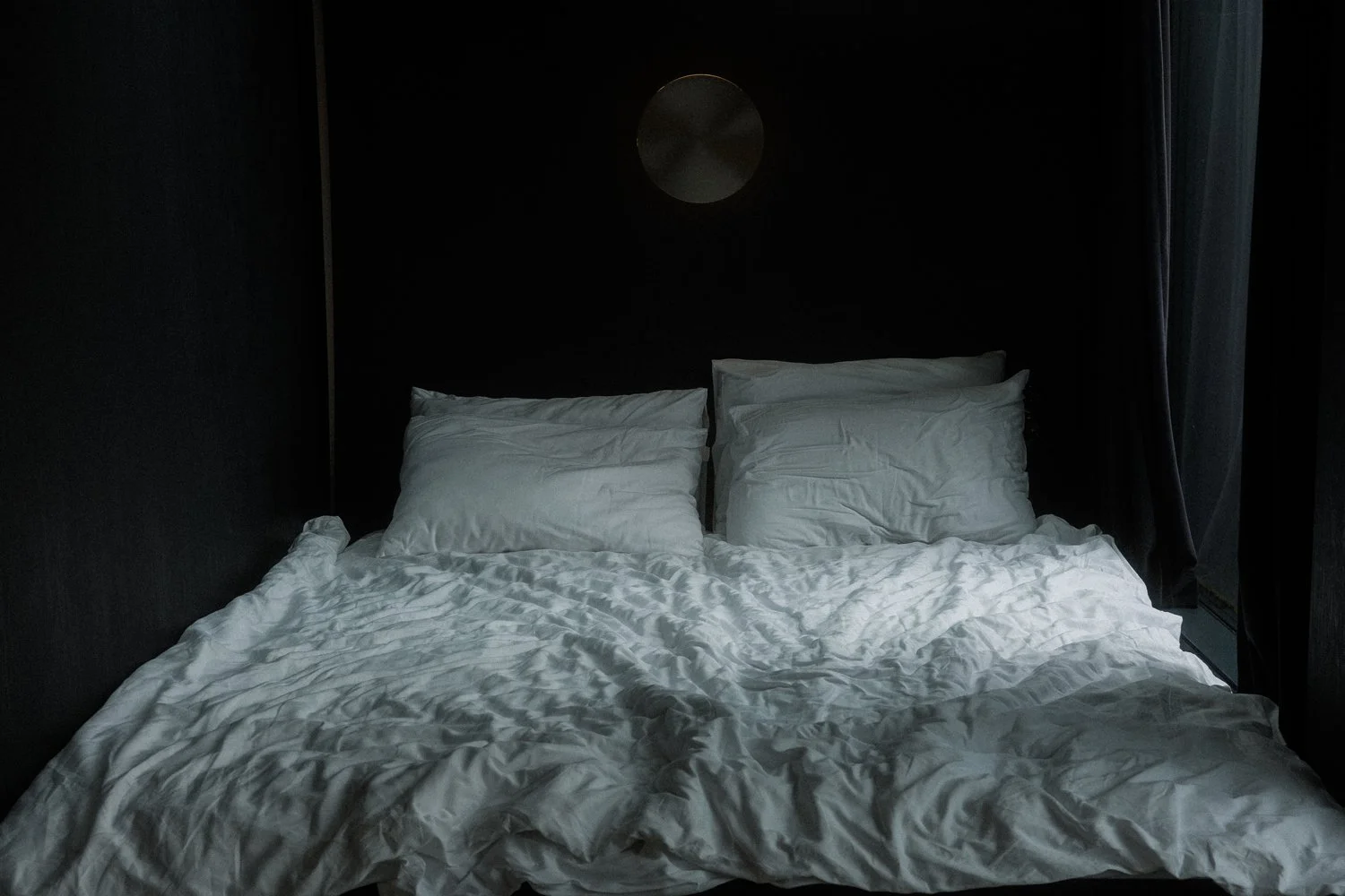 Unmade bed with white bedding and pillows in a dark room.