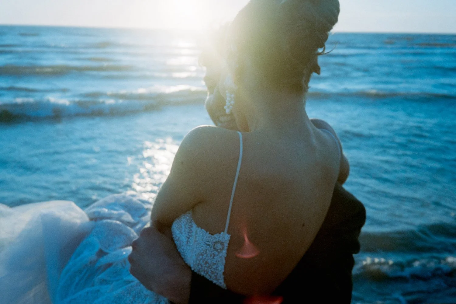 A woman in a swimsuit sitting by the ocean at sunset.
