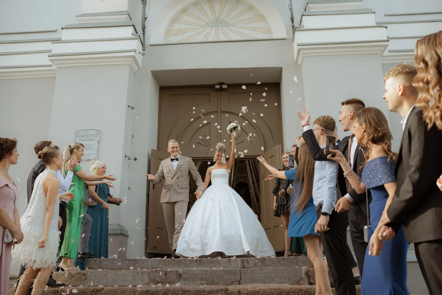 Bride and groom exiting a church surrounded by friends and family celebrating with confetti.