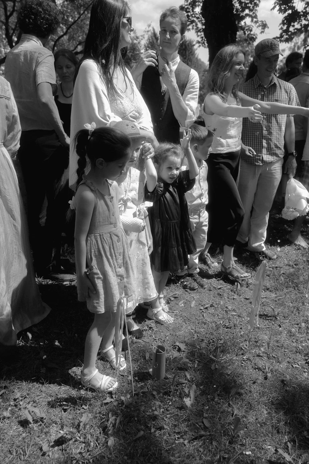 A group of children and adults gathered outdoors, possibly for a celebration or ceremony, with some children standing in the front and adults behind them, all engaged and smiling.