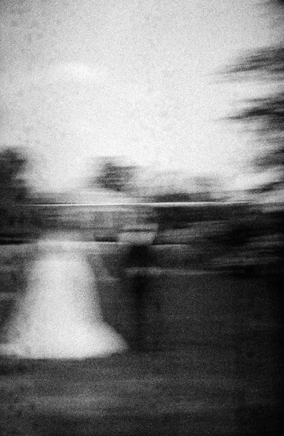 Black and white photo of a wuickly moving scene with blurred trees and a person in the foreground.