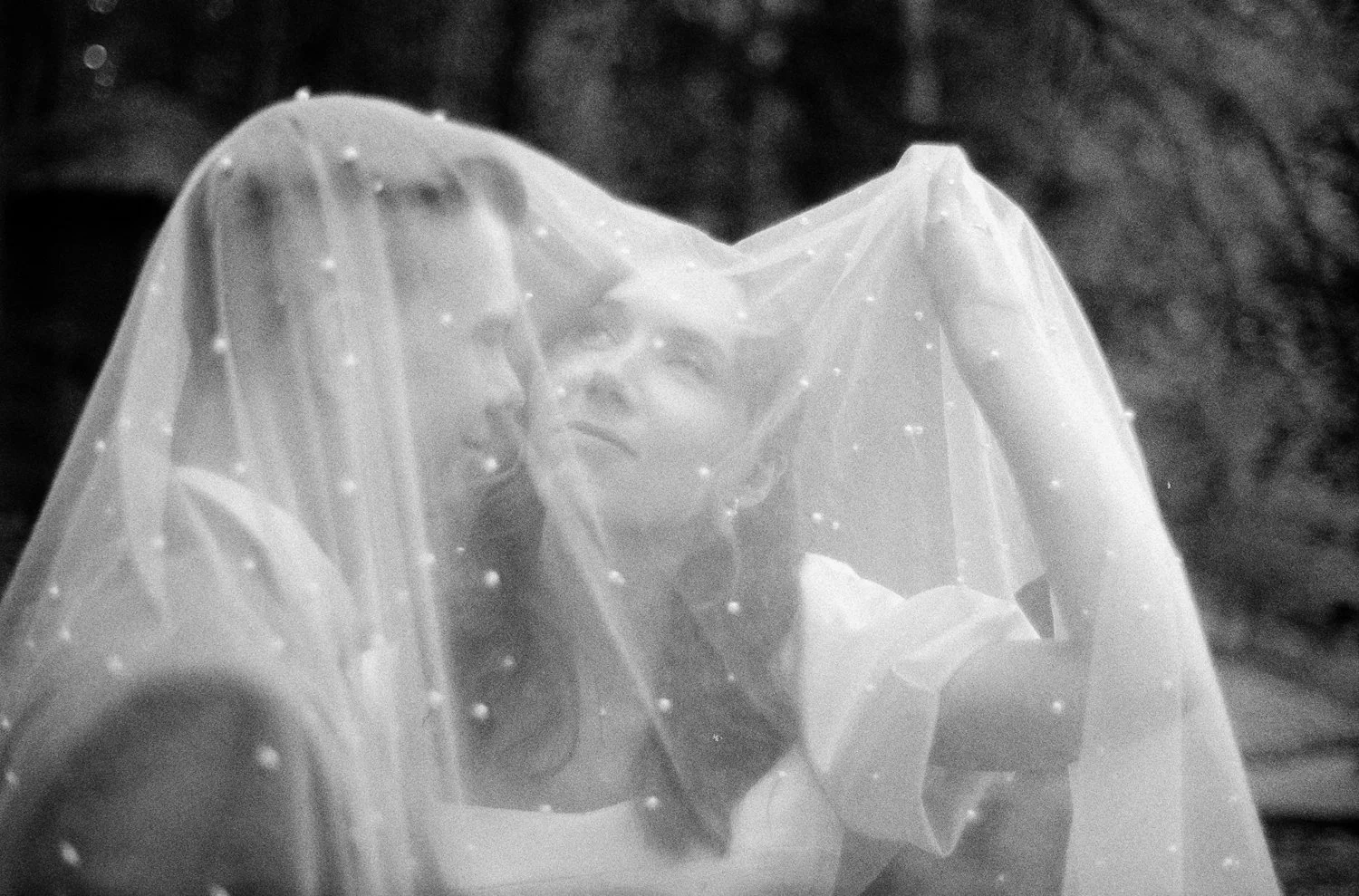 A woman looking through a sheer veil or fabric with small beads, with a blurred outdoor background.