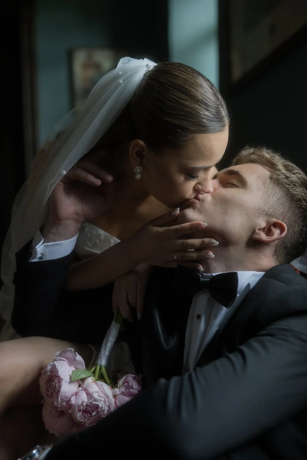 Bride and groom sharing a kiss, with the bride holding a pink bouquet of flowers.