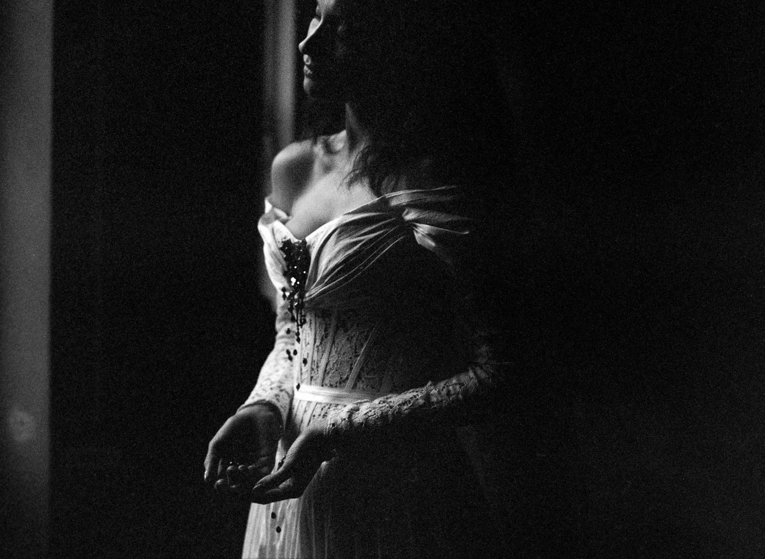 A woman in a lace and bead dress holding a baby, viewed in black and white, with a dark background.