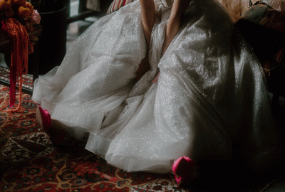 A person wearing a sparkling, metallic, silver-colored traditional dress, sitting on a patterned carpet.
