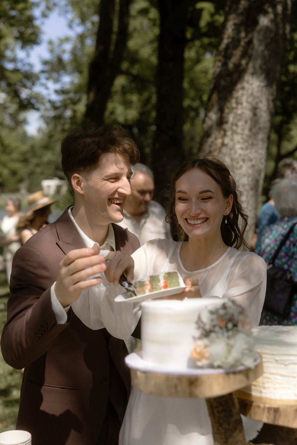 A wedding celebration outdoors with a couple cutting a cake and smiling.