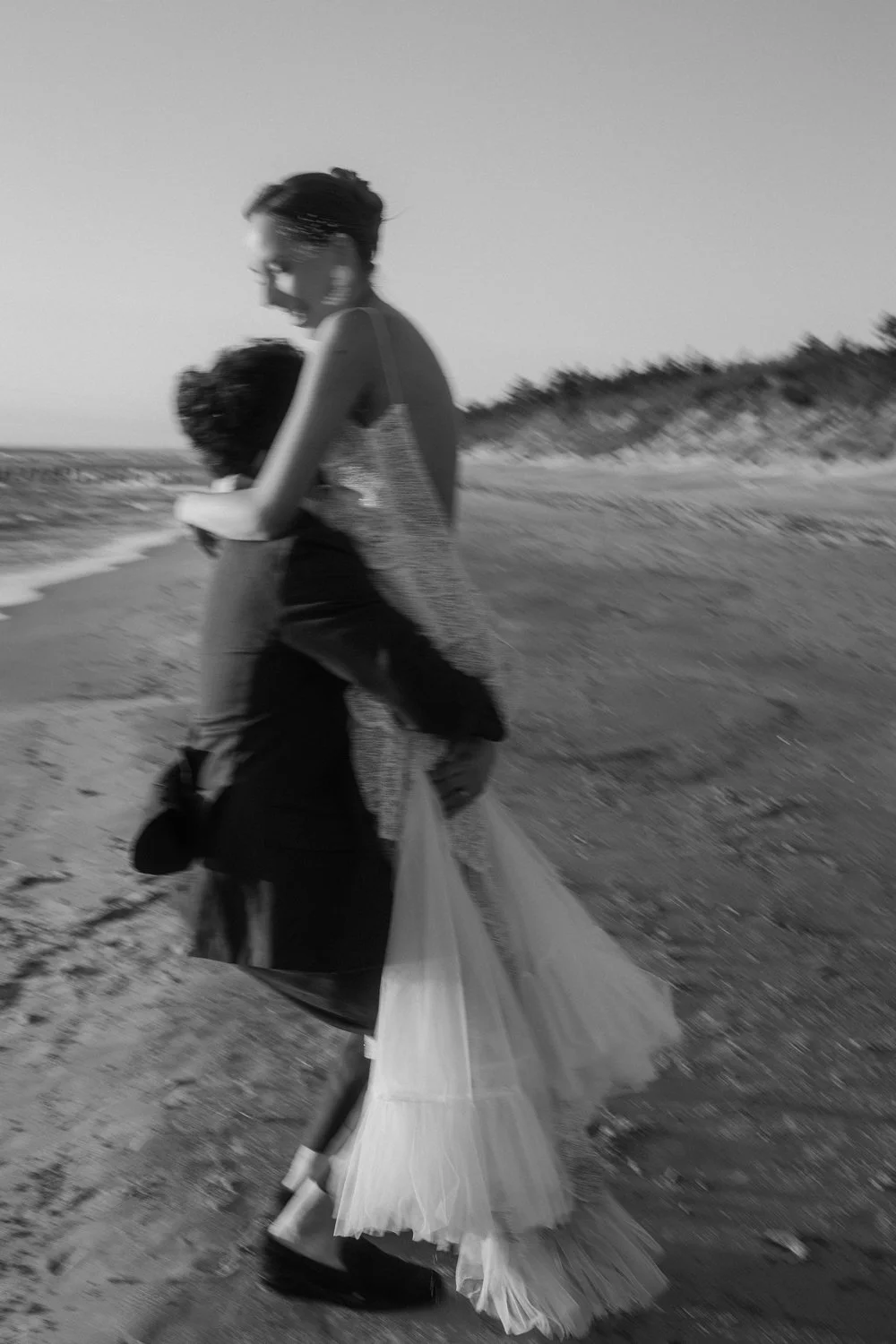 A woman and a child walking on the beach with the woman holding the child's hand, carrying a plastic bag, in black and white.