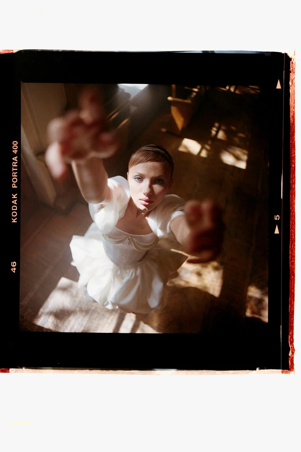 A woman in a white dress looking up at the camera, reaching out with her hand, taken from an overhead perspective.