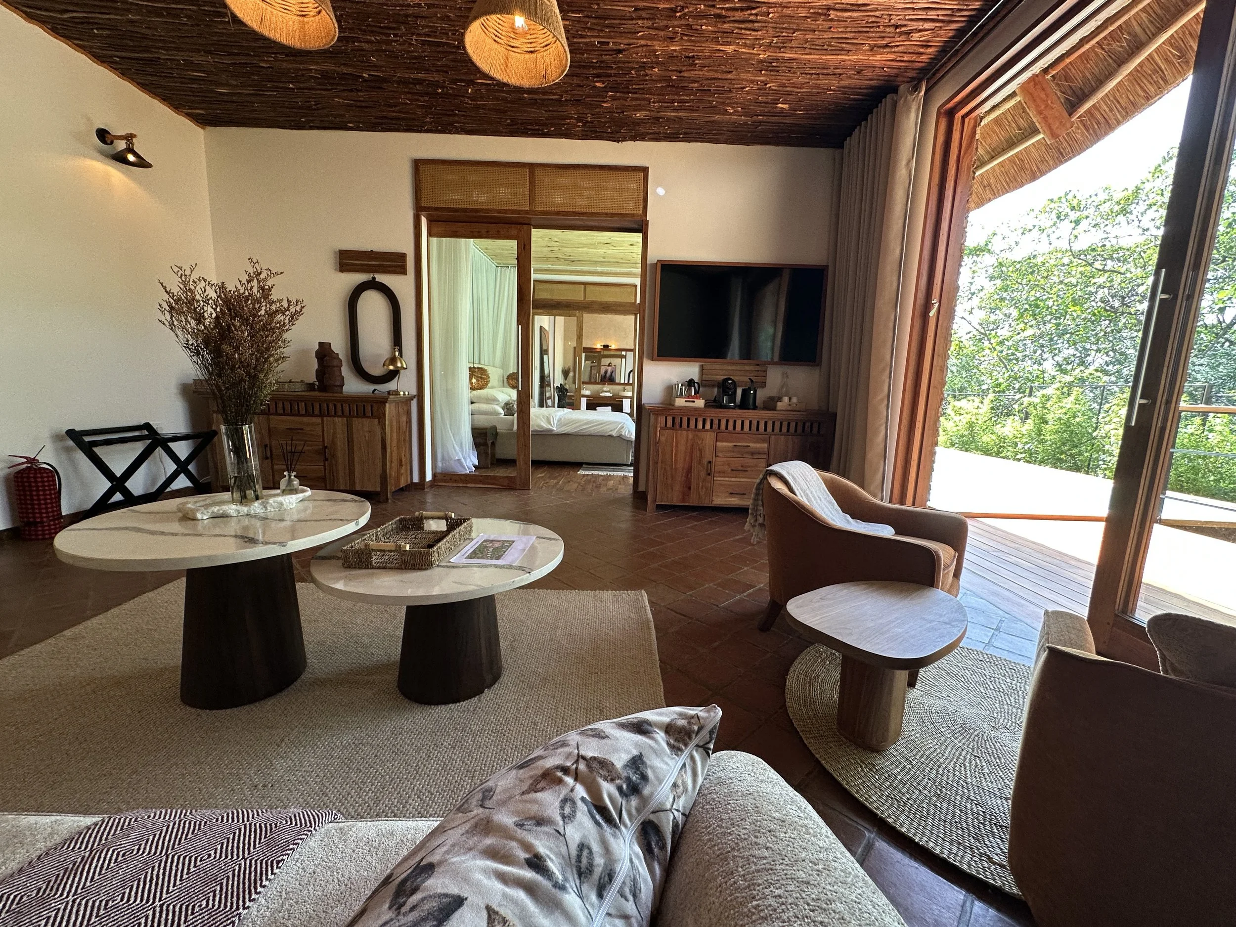 Living room with a sliding glass door leading to a balcony, a wall-mounted TV, wooden furniture, a beige sofa with decorative pillows, and a bedroom visible through an open doorway.