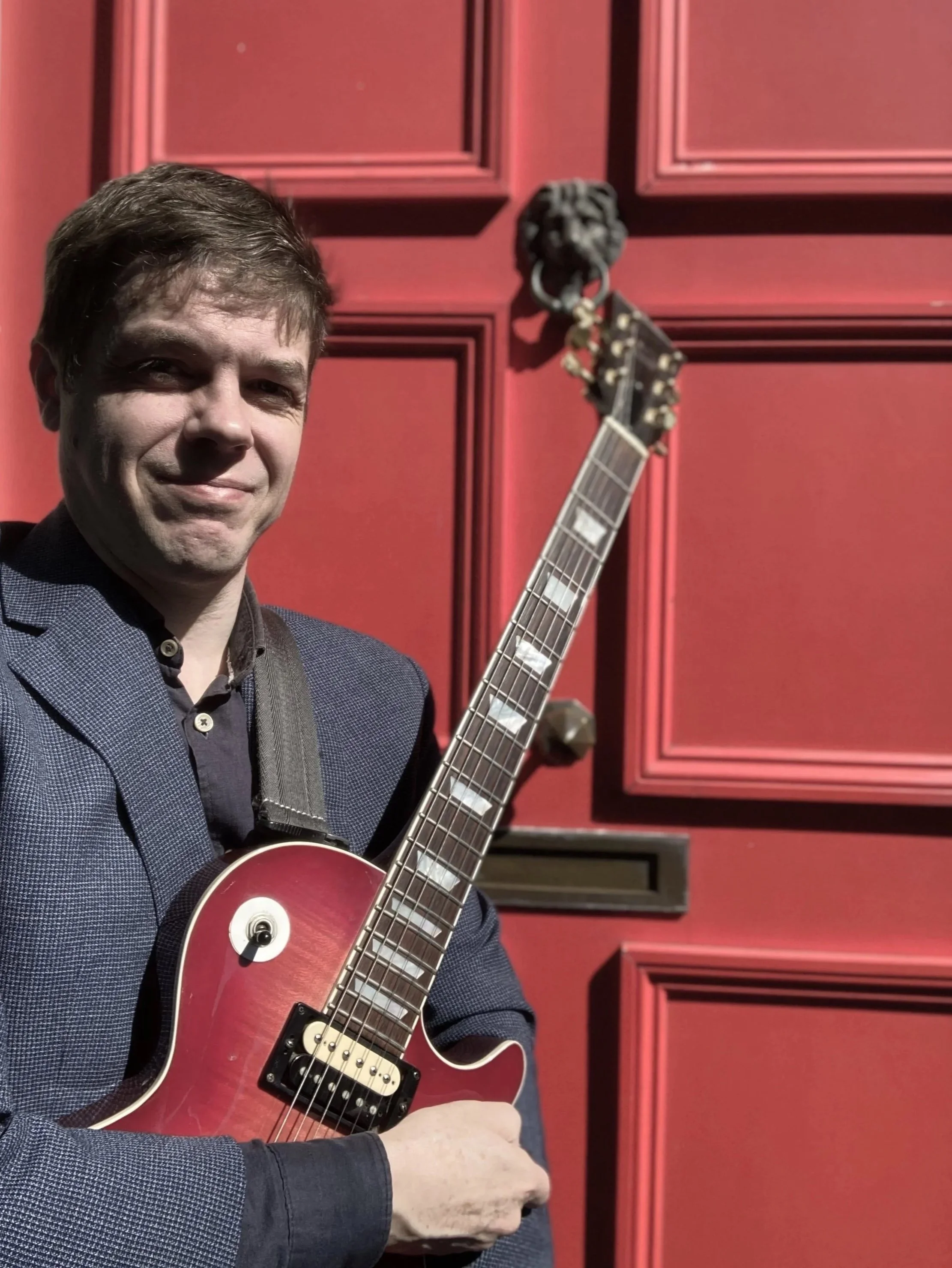 Guitar teacher holding electric guitar outside home studio in Bristol