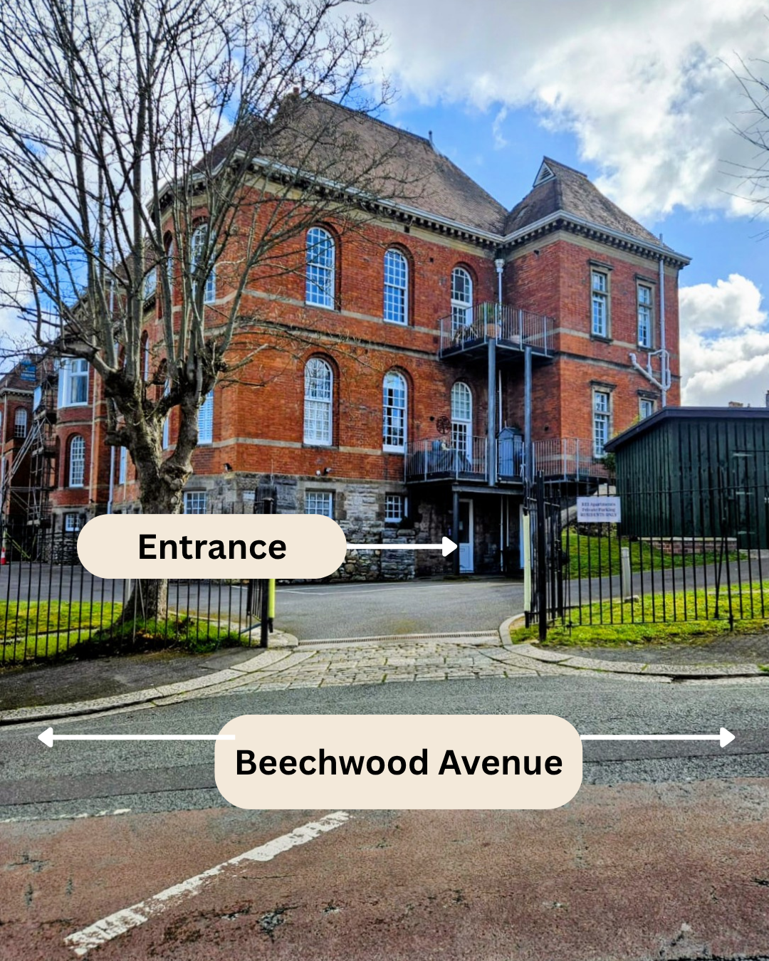 A brick building with multiple arched windows, a stone foundation, and a fire escape on the side. The building is behind a black metal fence. There is a tree and a green shed nearby. The sky is partly cloudy. Labels indicate the entrance gate and Beechwood Avenue in front of the building.