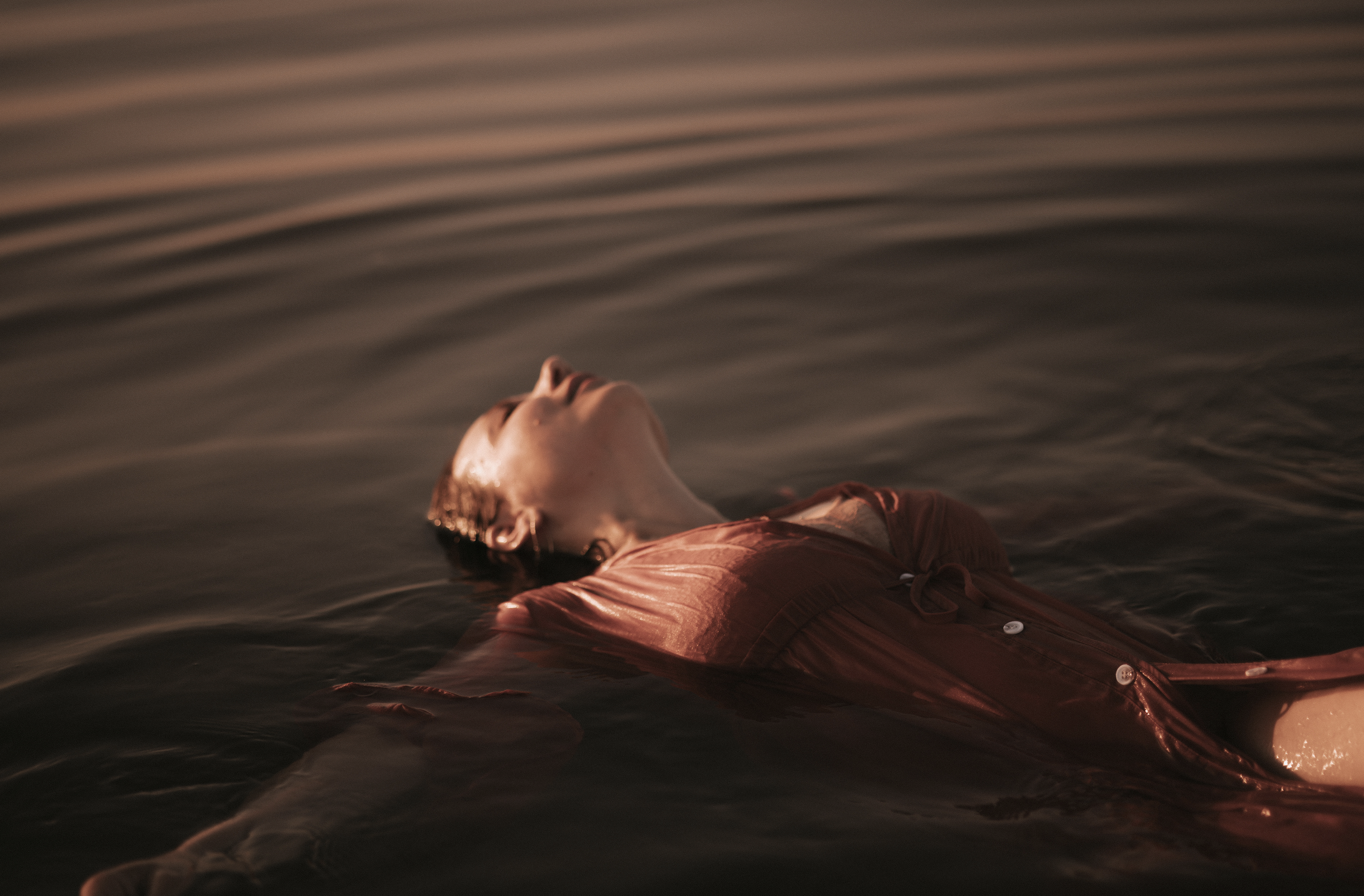 Frau liegt mit geschlossenen Augen entspannt in stiller, dunkler Wasseroberfläche.