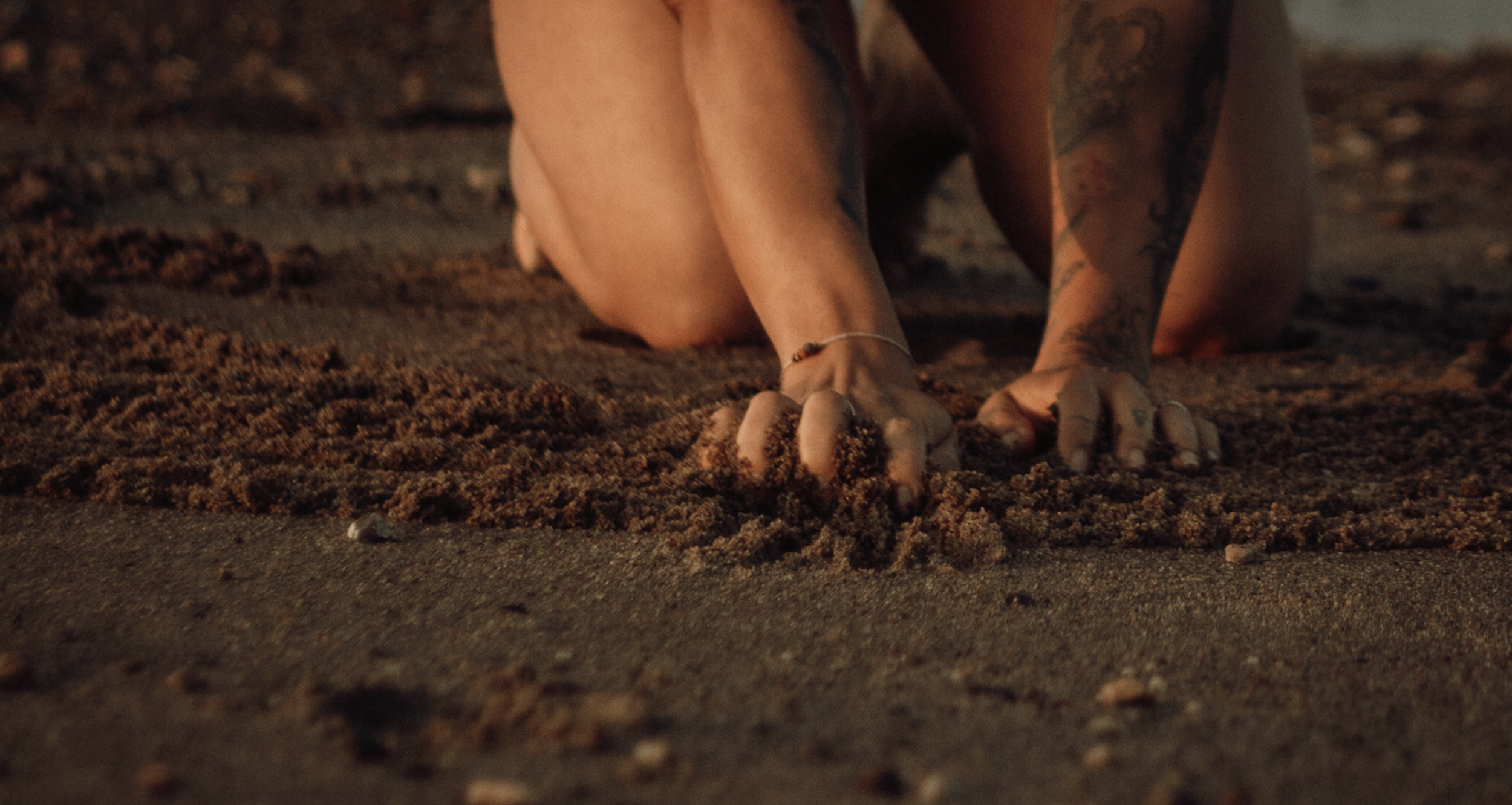 Person kniet auf dem Sandstrand und grabt Sand mit den Händen