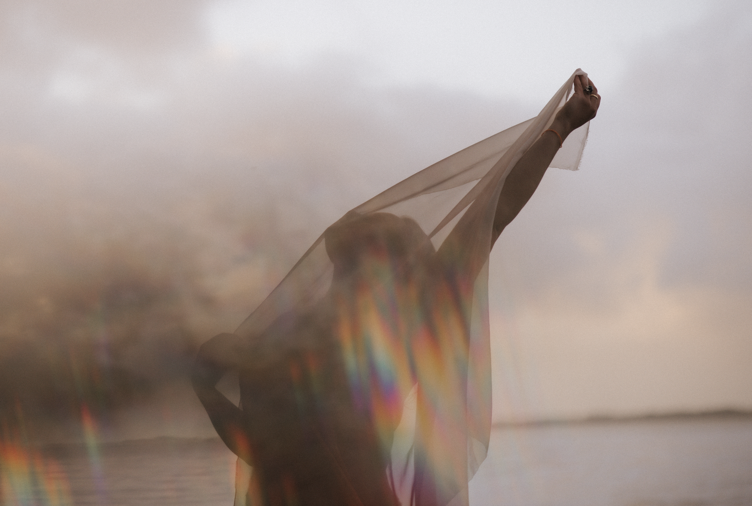 Eine Person, die einen durchsichtigen Stoff über dem Kopf hält, im Freien bei Dämmerung oder Sonnenuntergang, mit einem trüben Himmel im Hintergrund.